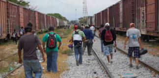 People walking along train tracks carrying backpacks