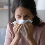 Woman sneezing into a tissue indoors