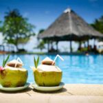 Two coconut drinks with straws beside a swimming pool