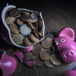 Shocking Retirement Drain – 1/3 Americans Cash Out! A broken pink piggy bank with coins spilling out onto a wooden surface