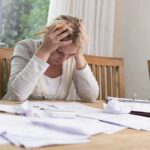 83% Face CRUSHING Money Reality — Shocking! A woman sitting at a desk with her head in her hands, surrounded by paperwork