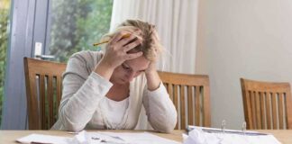 A woman sitting at a desk with her head in her hands, surrounded by paperwork