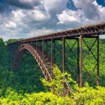 A large metal bridge spanning a lush green valley under a cloudy sky