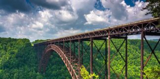 A large metal bridge spanning a lush green valley under a cloudy sky
