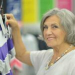 Senior woman smiling while holding a purple and gray shirt in a clothing store