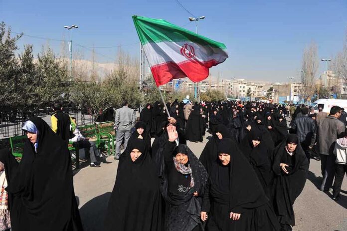 Group of women in black attire marching with an Iranian flag