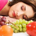 A woman resting her head on a table surrounded by various fruits