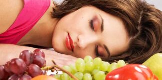 A woman resting her head on a table surrounded by various fruits