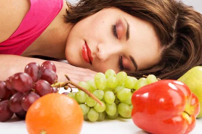 A woman resting her head on a table surrounded by various fruits