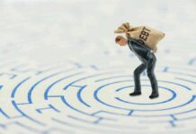 A miniature businessman carrying a sack labeled 'DEBT' in a maze