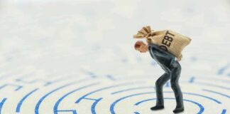 A miniature businessman carrying a sack labeled 'DEBT' in a maze