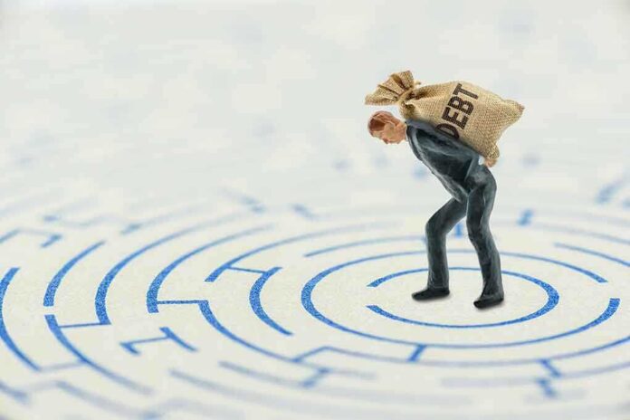A miniature businessman carrying a sack labeled 'DEBT' in a maze