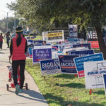 Is JFK’s Grandson a Political Maverick or Menace? Person walking with stroller past numerous election campaign signs.