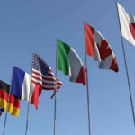 Flags of seven countries against clear blue sky.