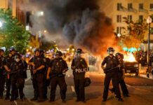 Bullets Fly — Brothers’ Daring Rescue Mission Police officers in riot gear near burning car.