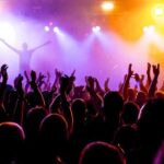 TERRIFYING Moment — Star Collapses During Live Show Crowd at a concert with raised hands and colorful stage lights