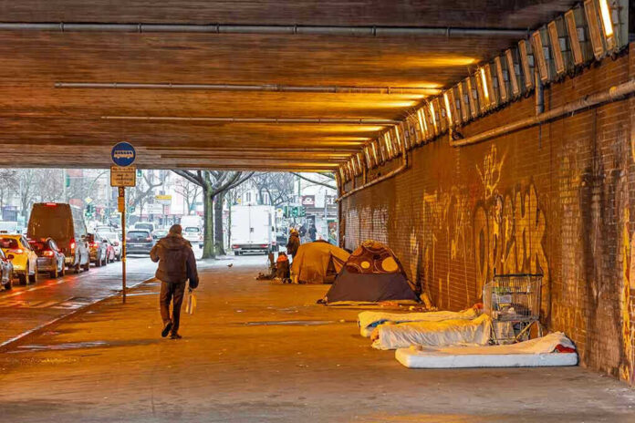 People walk under a bridge with homeless encampment.