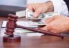 A person counting cash in a courtroom setting with a gavel in the foreground
