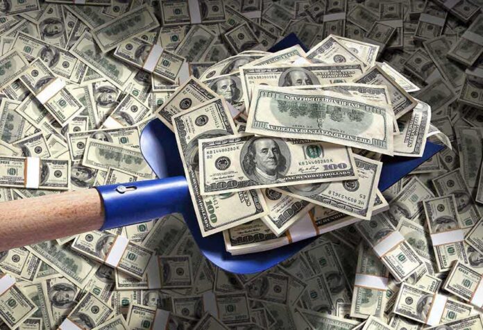 shutterstock_186500258.jpg A shovel filled with stacks of cash on a background of scattered dollar bills