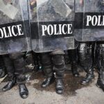 Barricaded Gunman UNLEASHES 36 Rounds On Police Police officers in riot gear standing behind shields marked POLICE