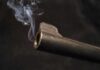 Close-up of a gun barrel emitting smoke against a black background