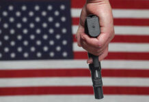 ICE Officer’s Bold Action SAVES Lives in L.A. Hand holding gun with American flag background.