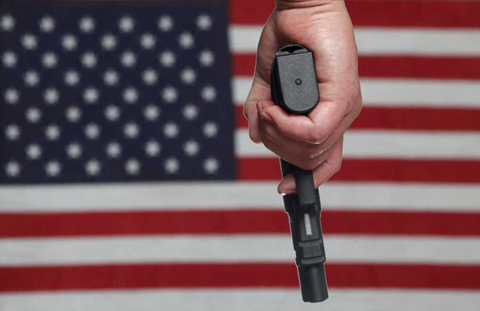 141984028 Hand holding gun with American flag background.