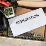 Envelope labeled RESIGNATION atop office supplies in box.