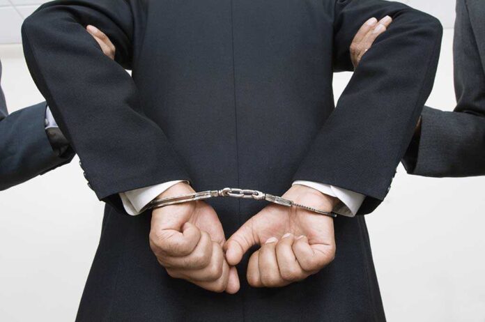 shutterstock_121141399.jpg A person in a suit with hands cuffed behind their back