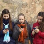 Three teenagers using smartphones while standing against a textured wall