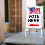 Voter ID Backlash: Hidden Agenda Uncovered Vote Here sign with arrow and American flag.
