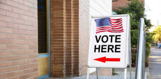 Vote Here sign with arrow and American flag.