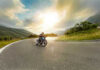 Person rides motorcycle on curved mountain road at sunset.