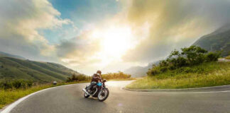 Person rides motorcycle on curved mountain road at sunset.
