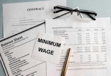 Trump’s Economy CRUSHES Predictions Documents and glasses on table with Minimum Wage paper.