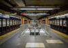 Subway station platform with directional signs overhead.