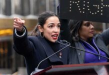 A woman passionately speaking at a rally with a sign in the background