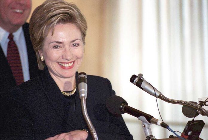 A smiling woman at a podium with microphones, speaking to an audience