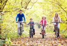 A family of four riding bicycles on a leafy path during autumn