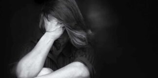 A person sitting with their knees drawn up, covering their face with their hands, expressing emotional distress.