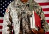 A soldier in a U.S. Army uniform holding books in front of an American flag
