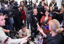 A crowded press conference with journalists and cameras surrounding a speaker