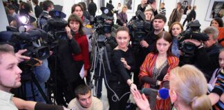 A crowded press conference with journalists and cameras surrounding a speaker