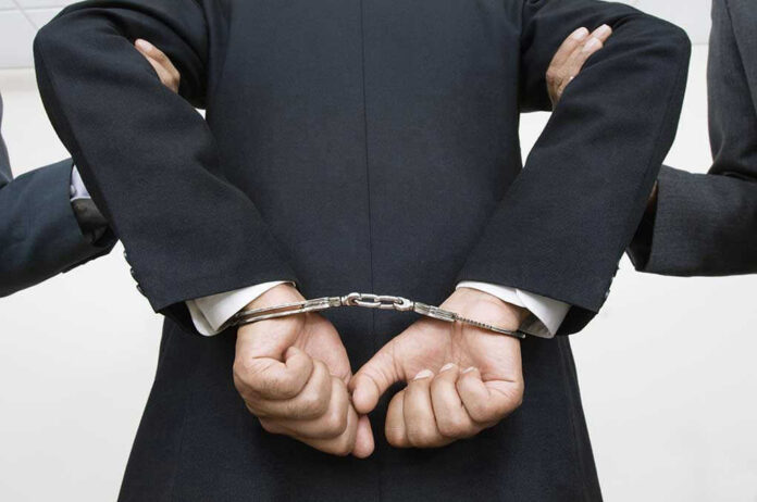 121141399 Person handcuffed in suit, escorted by two others.