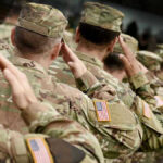 Soldiers in camouflage uniforms saluting in formation outdoors