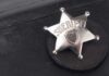 DETECTIVE AMBUSHED — Sheriff’s Brutal Response Stuns Nation A silver sheriff badge resting on a black leather surface