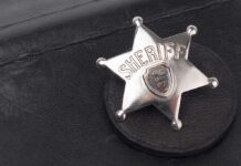 A silver sheriff badge resting on a black leather surface