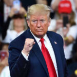 Trump Shakes GOP: Paxton Endorsement Stuns Party Man in suit making a fist gesture at rally.