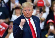 Trump Shakes GOP: Paxton Endorsement Stuns Party Man in suit making a fist gesture at rally.