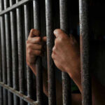 Hands gripping jail cell bars.